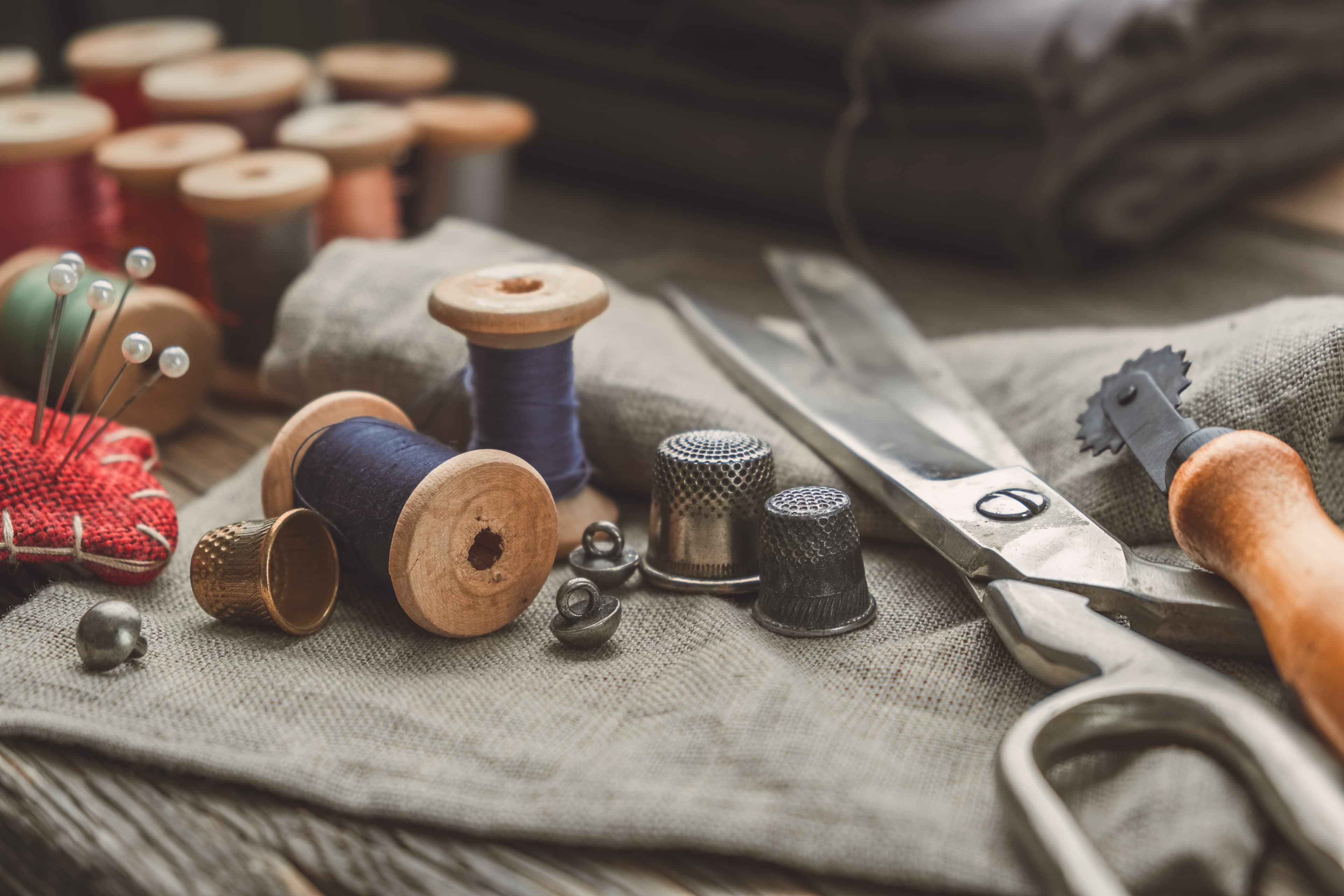 Tailor's bench — wooden thread spools, brass thimbles, shears and pinned linen